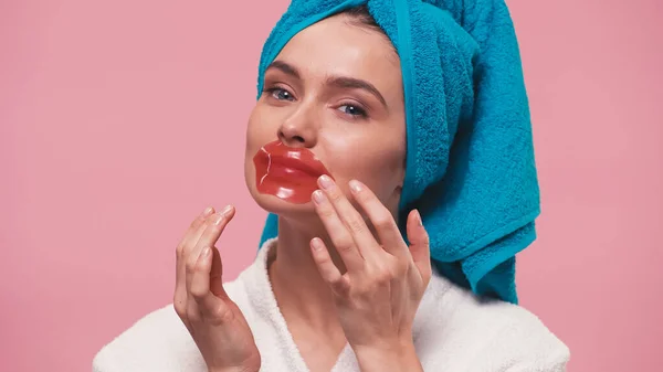 Pretty woman in terry bathrobe on head applying lip mask isolated on pink — Stock Photo