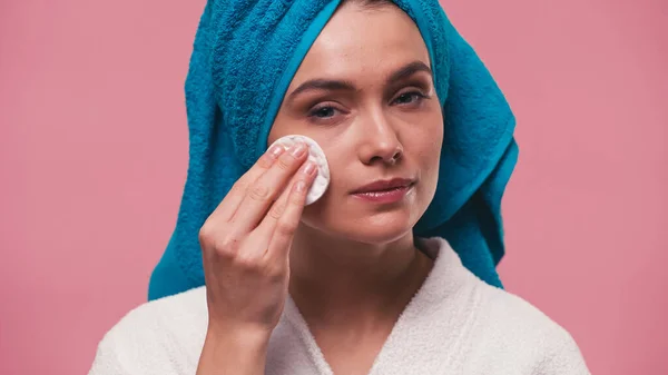 Femme avec serviette éponge sur la tête essuyant visage avec coton isolée sur rose — Photo de stock