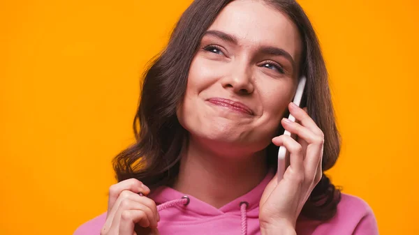 Mujer alegre mirando hacia otro lado mientras habla en el teléfono inteligente aislado en amarillo - foto de stock