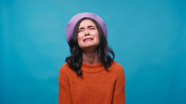 Traurige Frau in warmem Pullover und Baskenmütze weint vereinzelt auf blauem Grund — Stockfoto