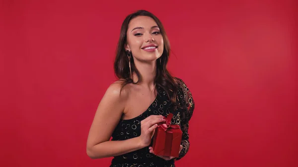 Веселая и элегантная женщина держит подарочную коробку изолированы на красный — стоковое фото