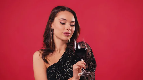 Young woman looking at glass of wine isolated on red — Stock Photo