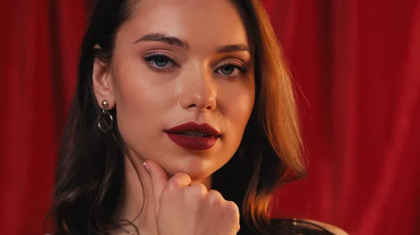 Bonita mujer joven con lápiz labial brillante mirando a la cámara en rojo - foto de stock