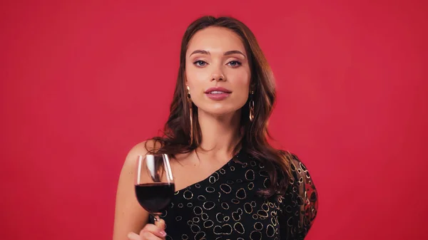 Elegant young woman holding glass of wine isolated on red — Stock Photo