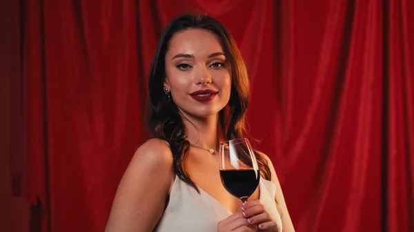 Jeune femme positive tenant un verre de vin sur rouge — Photo de stock