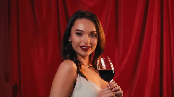 Усміхнена молода жінка тримає келих вина на червоному — стокове фото