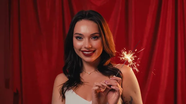 Happy woman with tattoo holding bright sparkler on red — Stock Photo