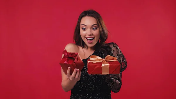 Взволнованная молодая женщина держит подарочные коробки изолированы на красный — стоковое фото