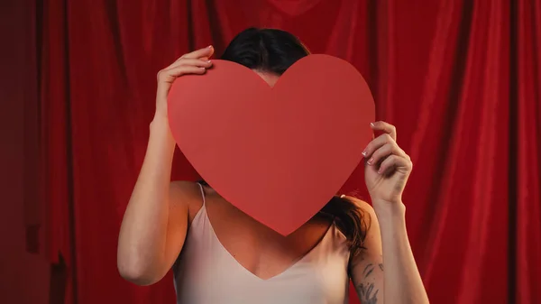 Jovem mulher segurando papel coração e rosto obscuro no vermelho — Fotografia de Stock
