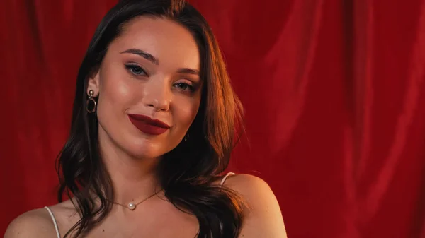 Young and pleased woman looking at camera on red — Stock Photo