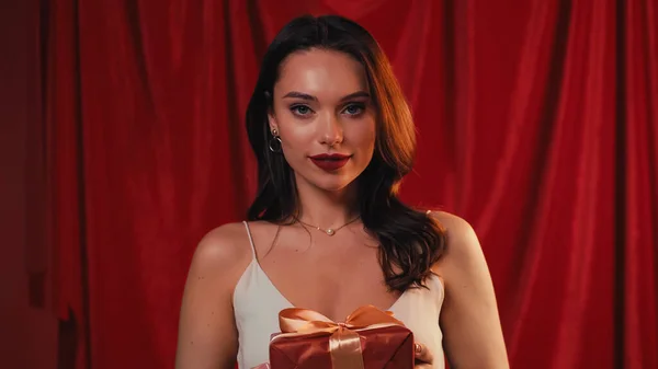 Heureux jeune femme tenant boîte cadeau sur rouge — Photo de stock