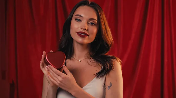 Femme tatouée tenant boîte en forme de coeur sur rouge — Photo de stock