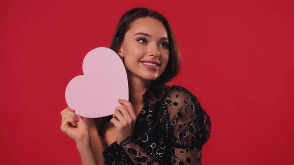 Elegante mujer sosteniendo el corazón de papel y sonriendo aislado en rojo - foto de stock