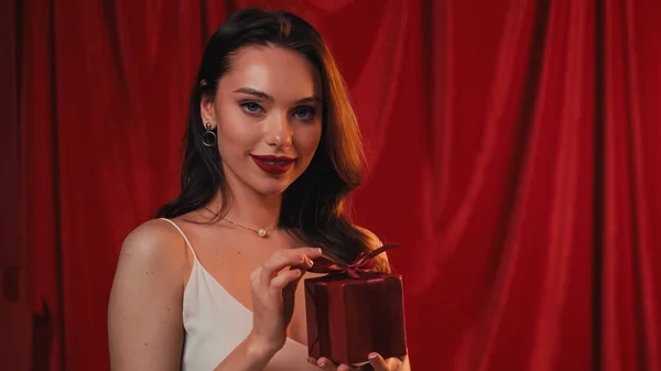 Mulher elegante sorrindo e segurando caixa de presente no vermelho — Fotografia de Stock