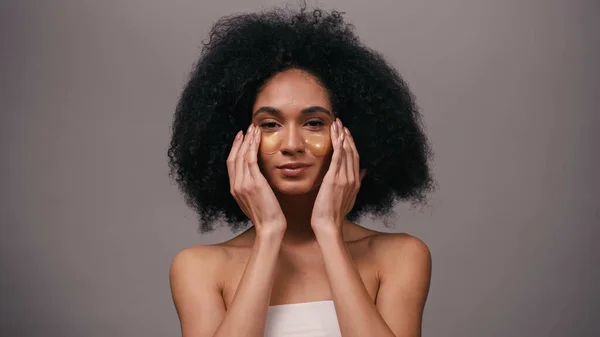 Curly african american woman with bare shoulders applying eye patches isolated on grey — Stock Photo