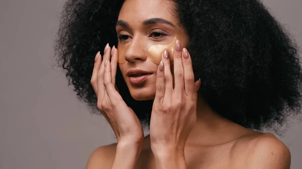 Mujer afroamericana aplicando parches oculares de colágeno aislados en gris - foto de stock