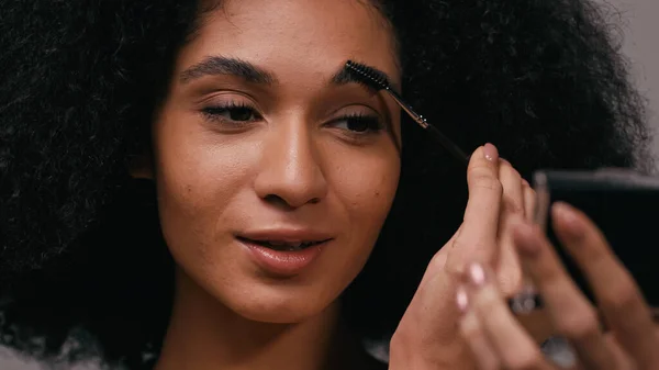 Gros plan de jeune femme afro-américaine brossant les sourcils isolé sur gris — Photo de stock