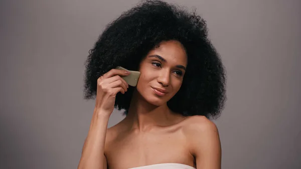 Mulher afro-americana com ombros nus usando jade gua sha stone isolado em cinza — Fotografia de Stock