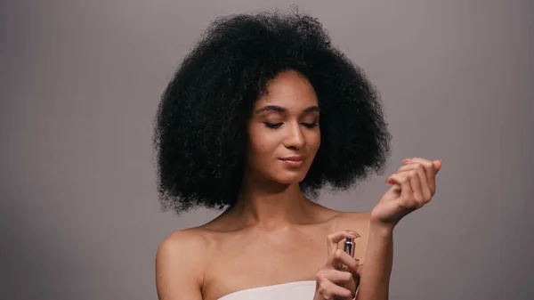 Joven afroamericana mujer rociando perfume en mano aislado en gris - foto de stock