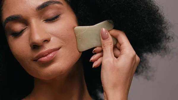 African american woman using gua sha stone isolated on grey — Stock Photo