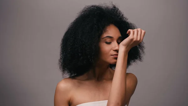 Joven afroamericana disfrutando de olor a perfume aislado en gris - foto de stock