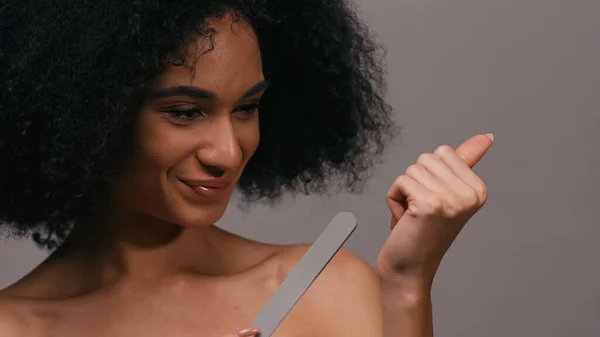 Donna afro-americana positiva utilizzando lima per unghie isolata su grigio — Foto stock