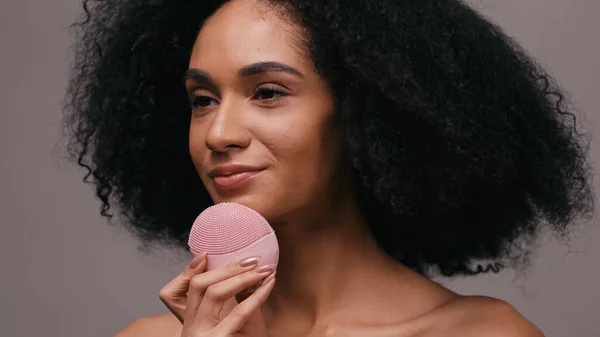 Jovem afro-americana usando dispositivo de limpeza de silicone no rosto isolado em cinza — Fotografia de Stock