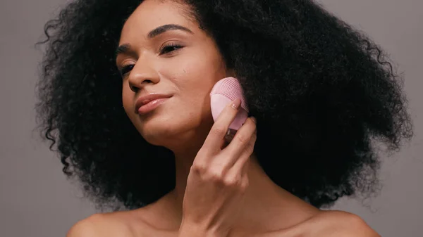 Mulher americana africana morena usando gadget de limpeza de silicone isolado em cinza — Fotografia de Stock