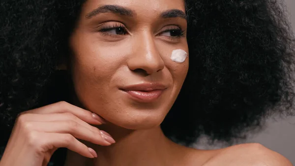 Gros plan de heureuse femme afro-américaine avec crème cosmétique sur le visage — Photo de stock