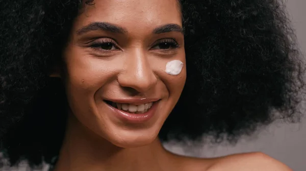 Mulher afro-americana positiva com creme cosmético no rosto — Fotografia de Stock