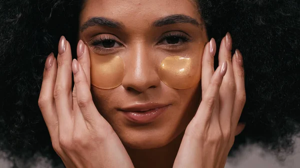Primer plano de la mujer afroamericana que aplica parches para los ojos - foto de stock