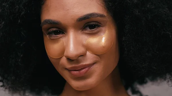 Primer plano de la mujer afroamericana feliz con parches de ojos hidratantes - foto de stock