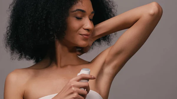 Positif femme afro-américaine appliquant déodorant isolé sur gris — Photo de stock
