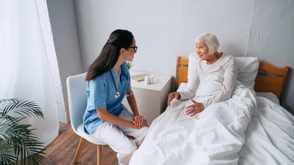 Infermiera in occhiali e sorridente donna anziana che parla in clinica — Foto stock