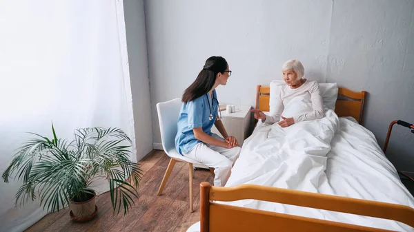 Altenpflegerin mit Brille und Seniorin im Gespräch in Klinik — Stockfoto