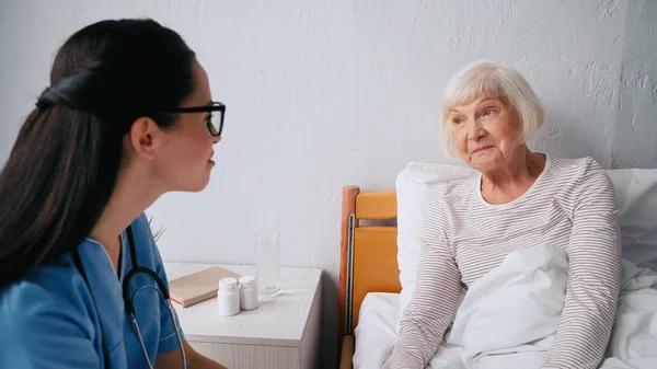 Розмита медсестра в окулярах біля старшої жінки в клініці — стокове фото