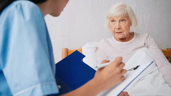 Enfermeira desfocada que escreve prescrição perto de mulher idosa — Fotografia de Stock