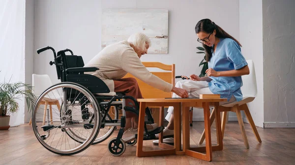 Enfermera joven y feliz mujer mayor jugando juego de mesa - foto de stock
