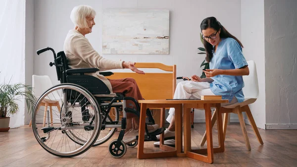 Enfermera joven y alegre mujer mayor jugando juego de mesa - foto de stock