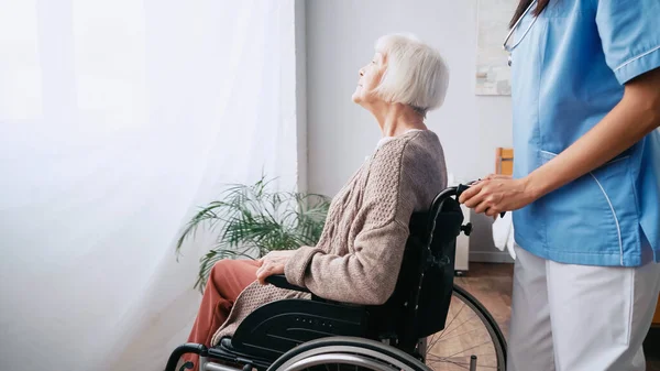 Altenpfleger bewegt betagte Frau im Rollstuhl — Stockfoto