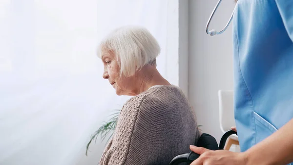 Altenpflegerin mit Stethoskop bewegt alte Frau im Rollstuhl — Stockfoto