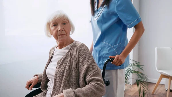 Infirmière avec stéthoscope femme âgée en mouvement en fauteuil roulant — Photo de stock