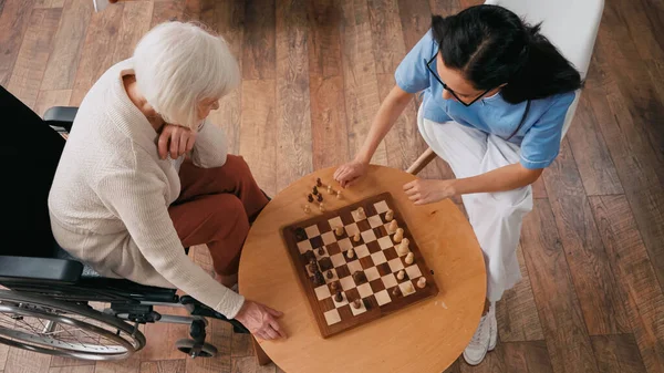 Вид пожилой женщины и медсестры, играющей в шахматы в доме престарелых — стоковое фото
