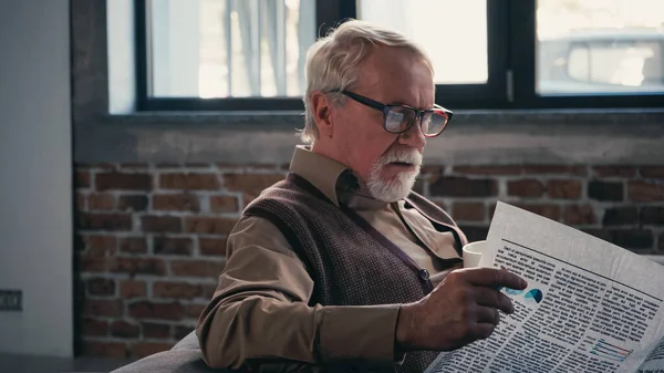 Homem idoso barbudo em óculos lendo jornal em casa — Fotografia de Stock