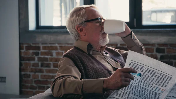 Homem idoso barbudo em óculos segurando jornal enquanto bebia chá — Fotografia de Stock