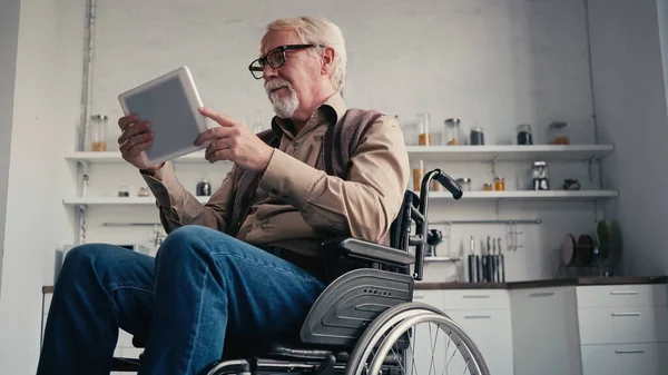 Pensionné handicapé en fauteuil roulant utilisant une tablette numérique à la maison — Photo de stock