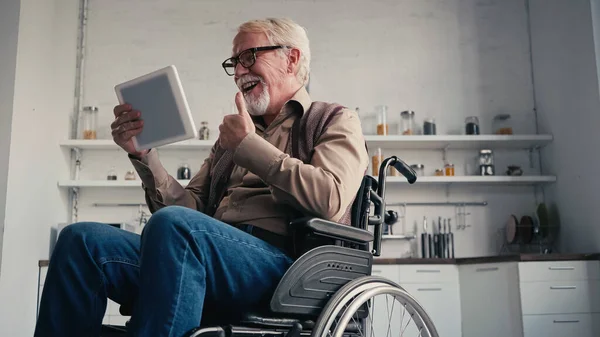 Smiling disabled pensioner in wheelchair showing thumb up during video call at home — Stock Photo