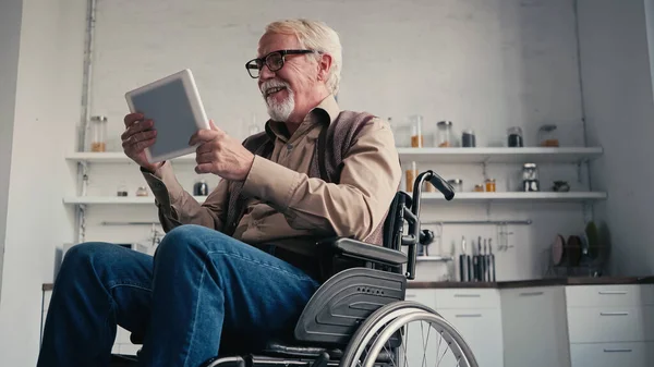 Веселый пенсионер-инвалид в инвалидной коляске с помощью цифрового планшета на дому — стоковое фото