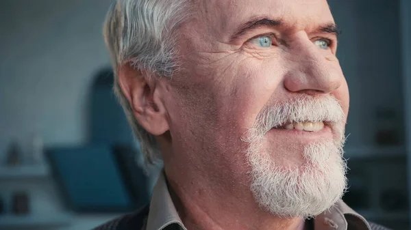 Close up of retired bearded man looking away while smiling at home — Stock Photo