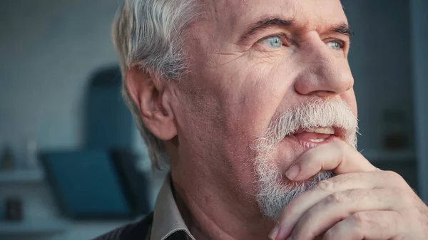 Close up of pensive and retired man looking away while touching face — Stock Photo